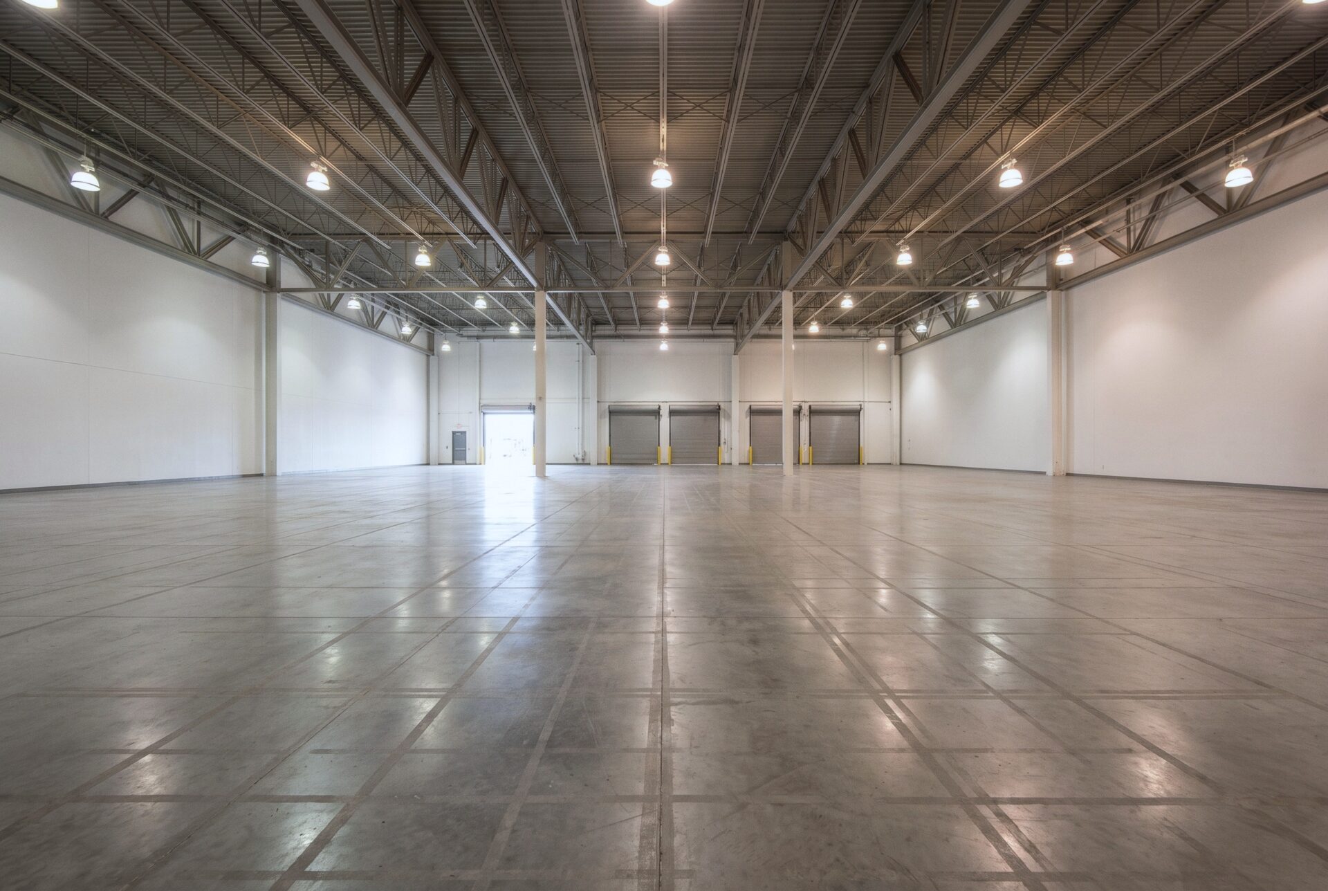 An empty exhibit hall with a polished concrete floor, steel trusses, and loading doors at the far end.