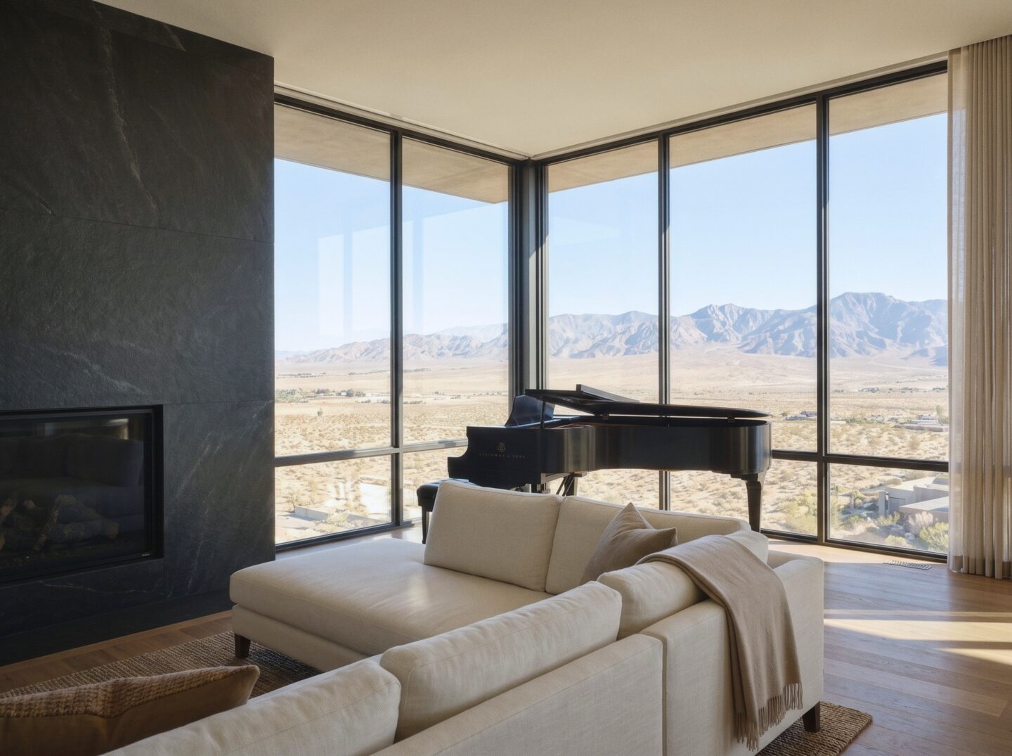 The Kona Penthouse living room on a hazy morning, with ivory sofas, a grand piano, and a corner window over the desert valley.