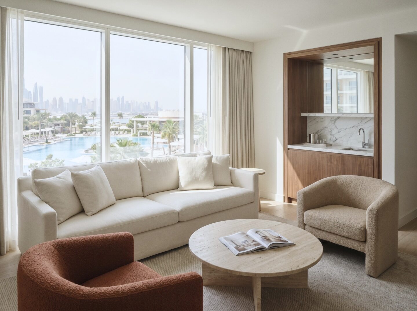 A Tower Suite living room with a linen sofa, a rust armchair, and a travertine coffee table beside windows over the pools and city.